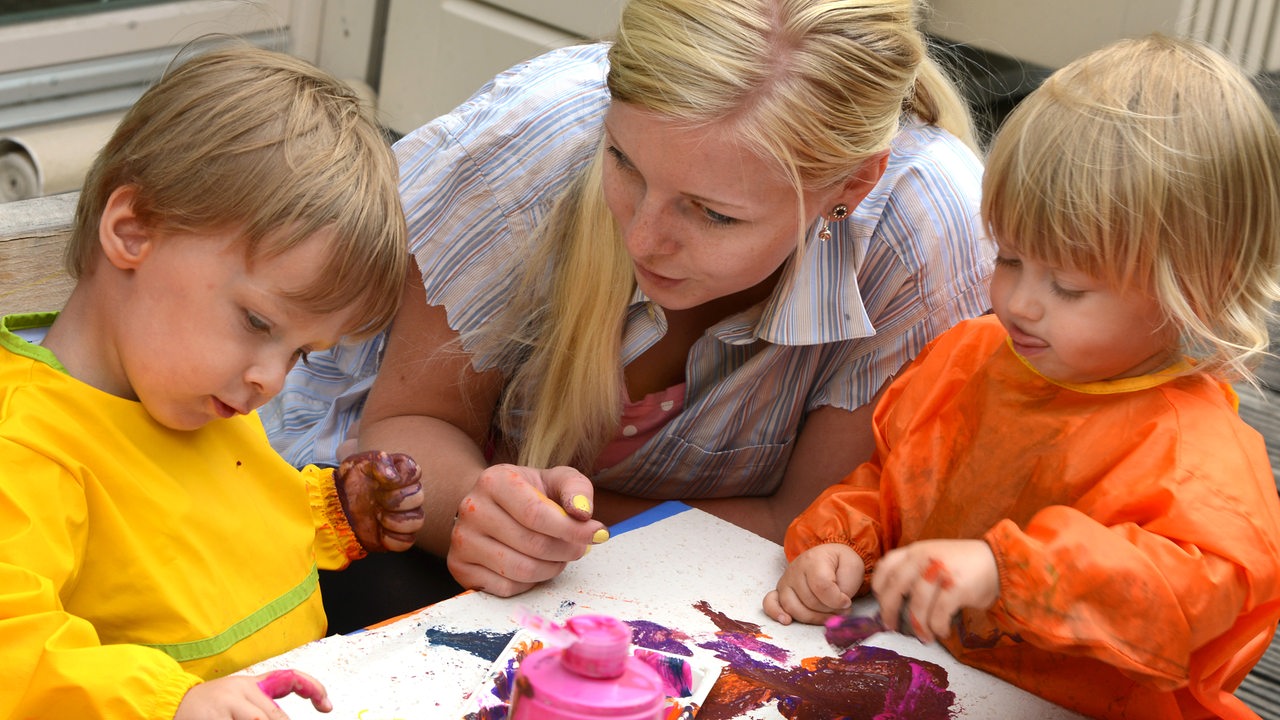 Ein junge Frau im freiwilligen sozialen Jahr malt mit Kindern in einer Kita.
