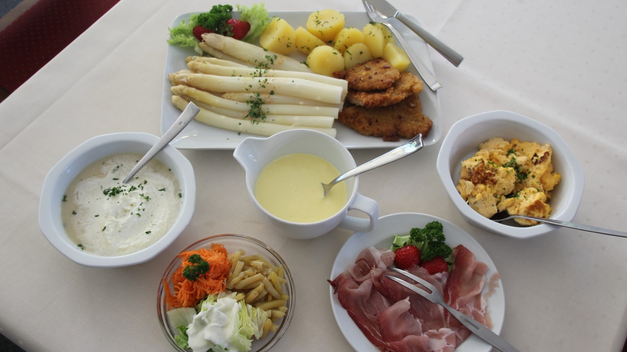 Ein Spargelmenü auf einem Tisch mit Salat, Kartoffeln, Schinken und Sauce Hollandaise