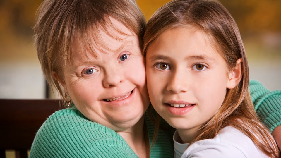 Zwei Mädchen, eines mit Trisomie 21, umarmen sich.