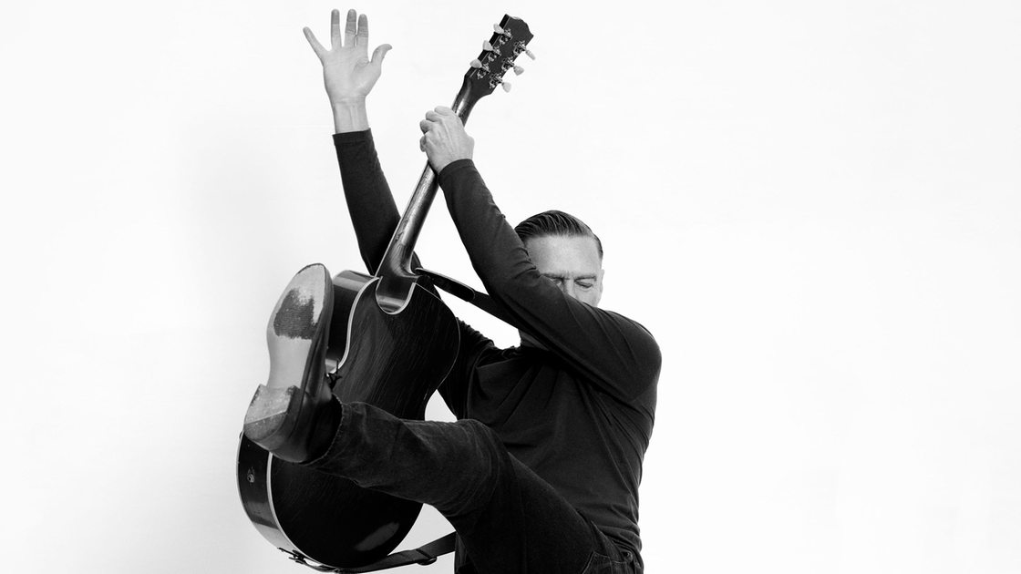 Der Musiker Bryan Adams mit Gitarre vor einem weißen Hintergrund