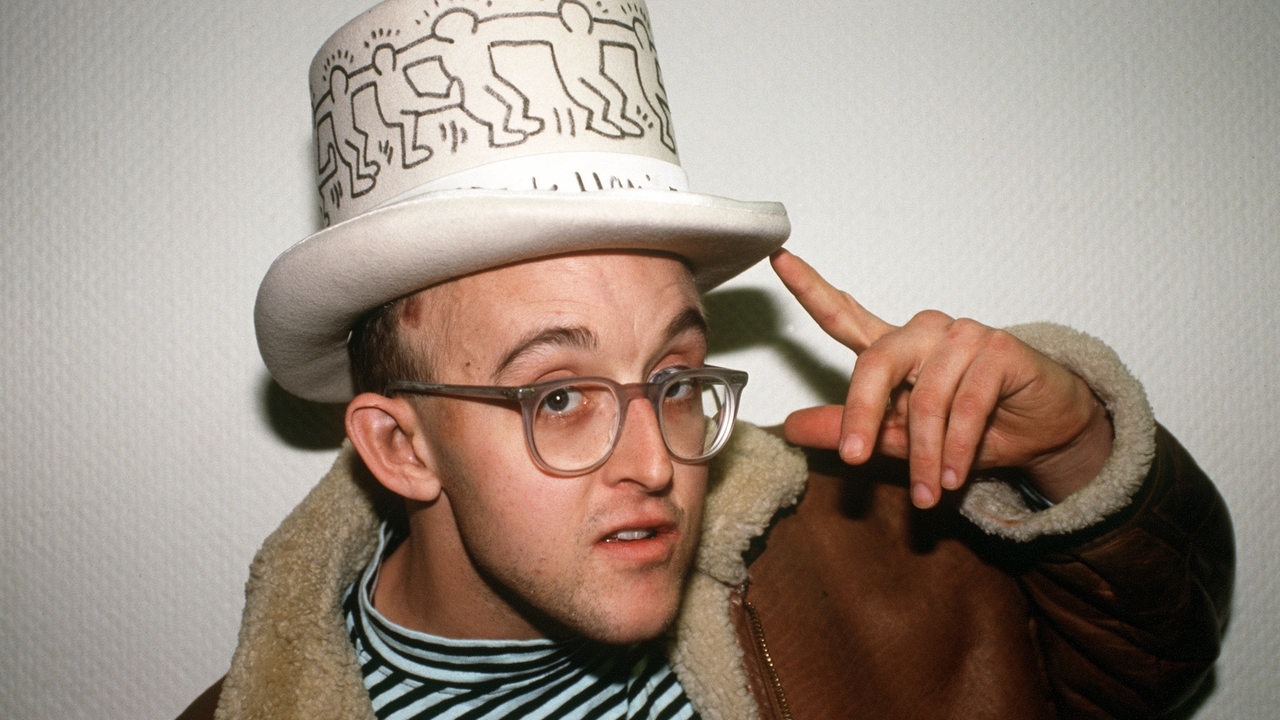 Der US-amerikanische Graffiti-Künstler Keith Haring posiert 1990 mit einem Zylinder-Hut, auf dem seine berühmten "Männchen" abgebildet sind.