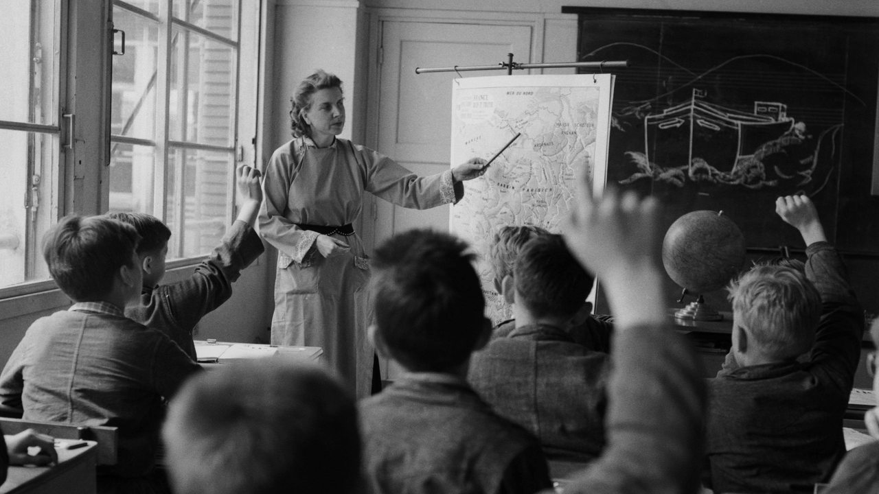 Historisches Foto einer Lehrerin, die vor der Klasse steht und etwas auf einer Karte zeigt.
