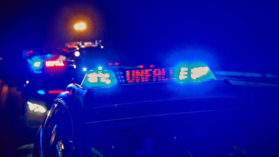 Zwei Polizeiwagen stehen in der Dunkelheit und die Leuchtschilder auf ihren Dächern sind erleuchtet. Auf ihnen steht Unfall geschrieben.