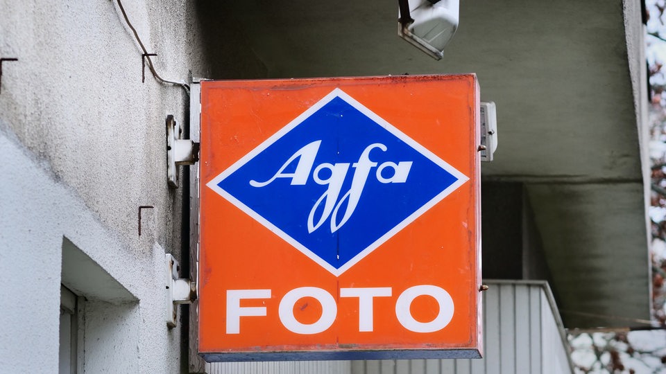 Ein altes Schild mit dem Schriftzug "Agfa Foto" hängt an der Wand eines Hauses.