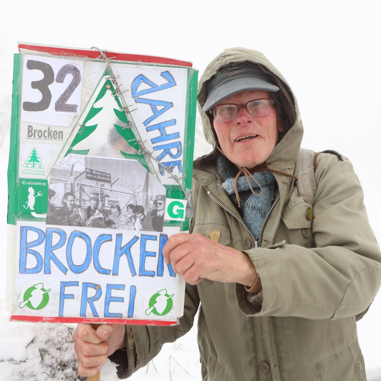 Wanderer Benno Schmidt, besser bekannt als Brocken Benno, steht mit einem Schild zur Erinnerung an die Brockenöffnung am 3.12.1989 auf dem Brocken. 