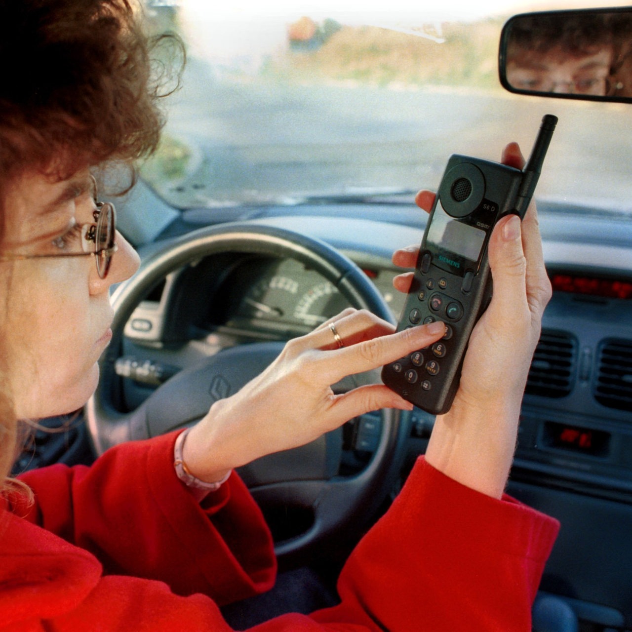 Eine Frau sitzt im Auto und tippt in ein Handy der frühen Generation