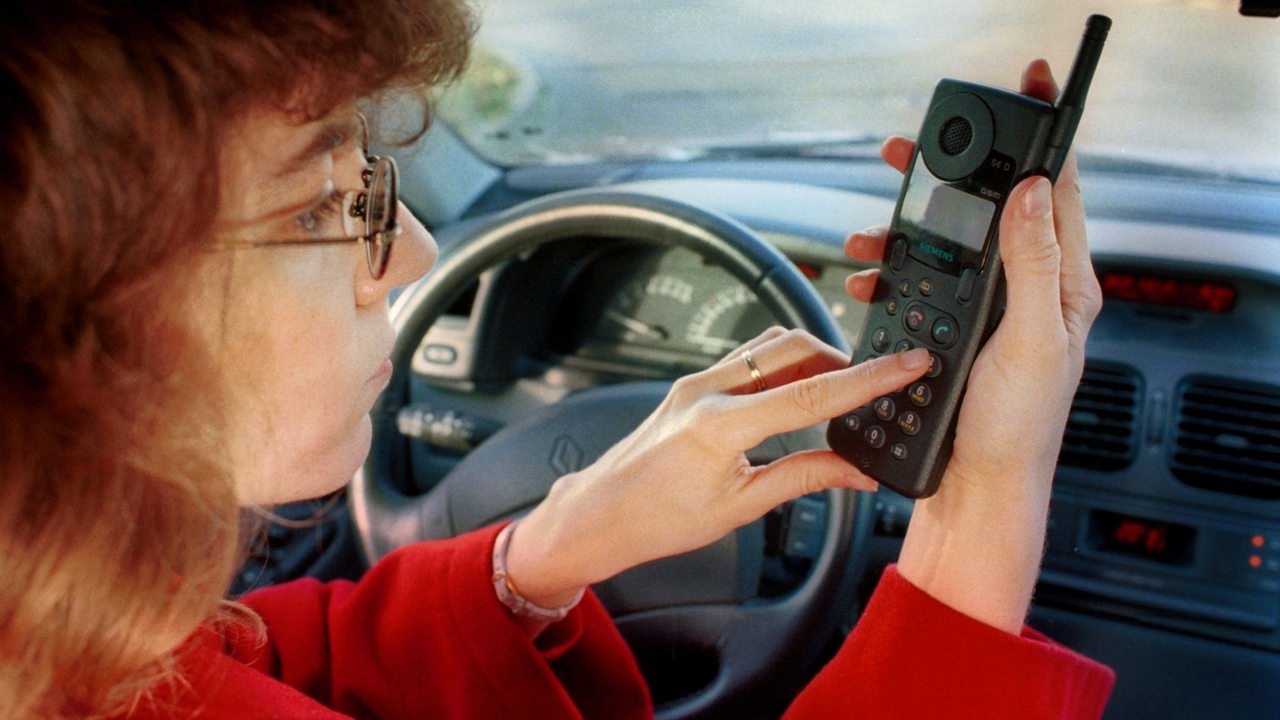 Eine Frau sitzt im Auto und tippt in ein Handy der frühen Generation