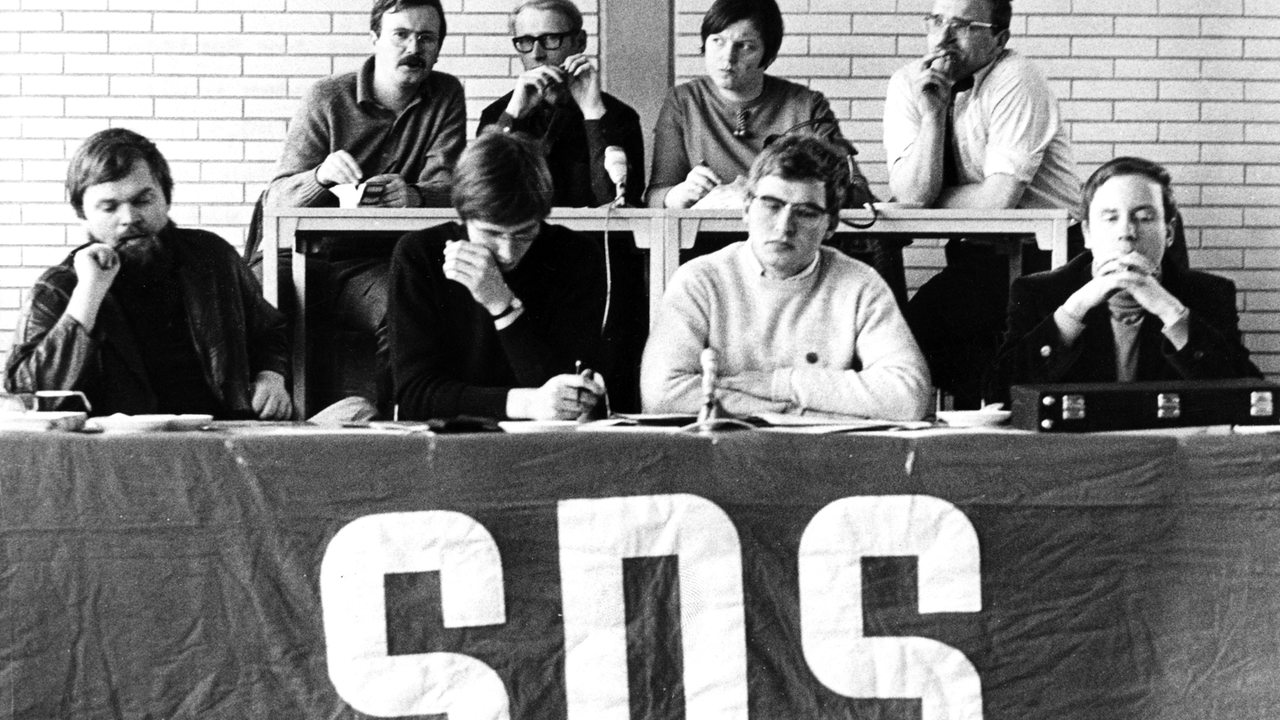 SDS Bundesvorstand von 1968, 8 Personen in zwei Reihen, am Tisch das Transparant SDS