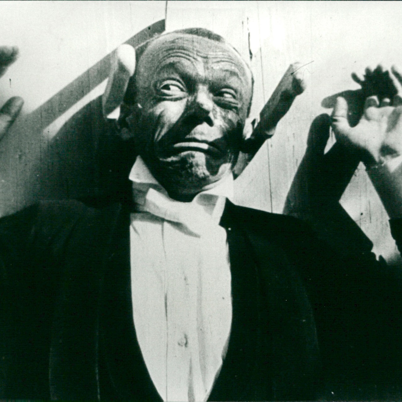 Der deutsche Komiker Karl Valentin in einer Filmszene an einer Wand mit Messern.