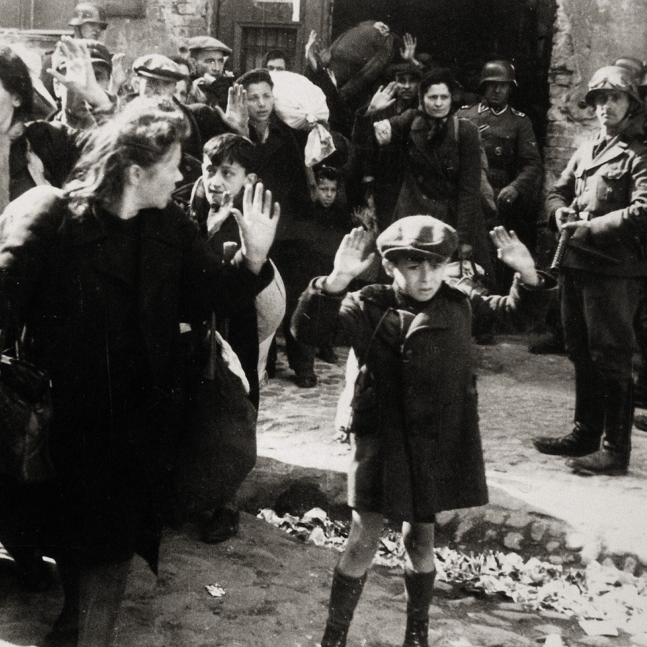 Warschauer Ghettoaufstand April/Mai 1943: Kleiner Bub mit erhobenen Händen, Frauen und andere Kinder kommen aus einem von den deutschen Truppen eroberten Haus. Aus dem Album von SS-Gruppenführer und Polizei-Generalmajor Jürgen Stroop. Photographie, 1943.
