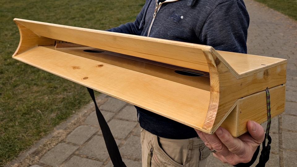 Ein Mann zeigt eine hölzerne Windharfe am Deich.