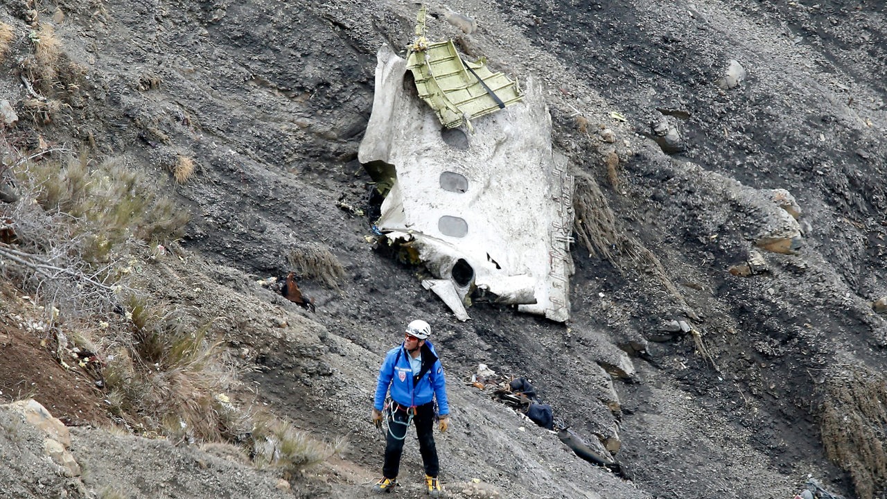 Ein Bergungshelfer steht am 25.03.2015 in der Nähe der Stadt Seyne-les-Alpes in Frankreich neben einem Trümmerteil des Germanwingsflugzeuges, dass in einem Hochgebirgstal der Alpen liegt.