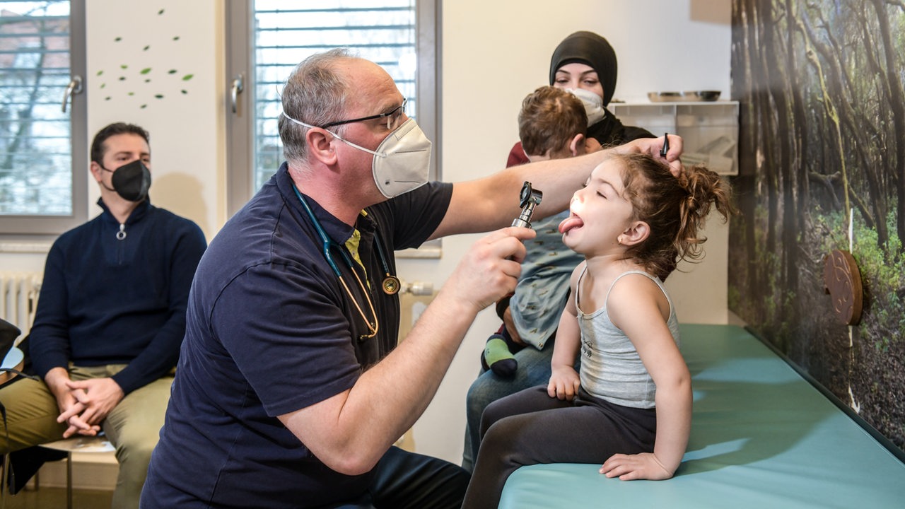 Ein Arzt mit Maske schaut einem Kind in den Hals.