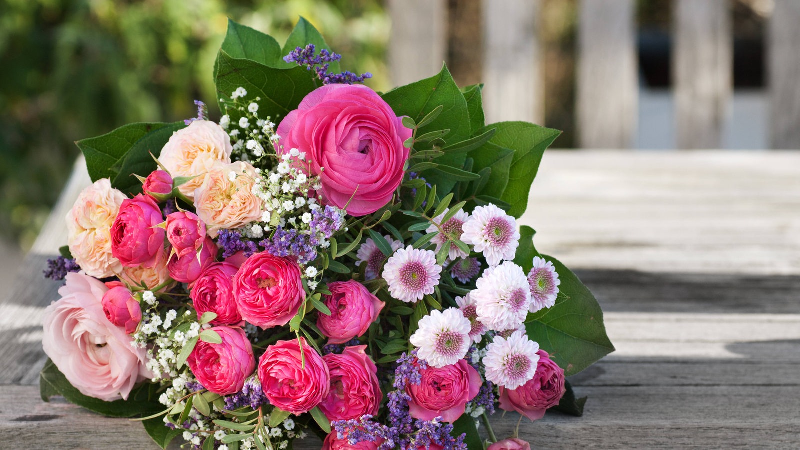 Ein buntere Blumenstrauß mit rosa und lila Blumen liegt auf einem Tisch