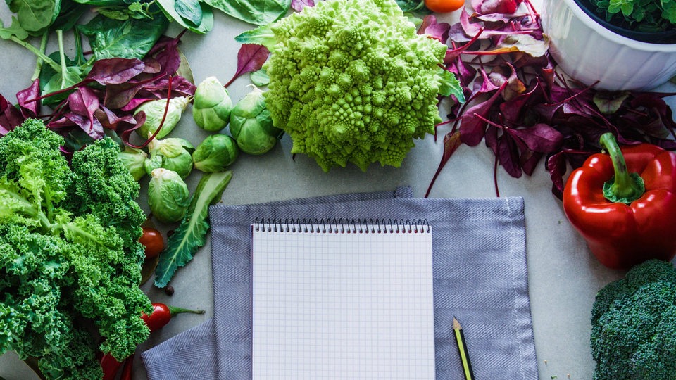 Verschiedenes Gemüse liegt rund um einen Notizblock mit Bleistift.
