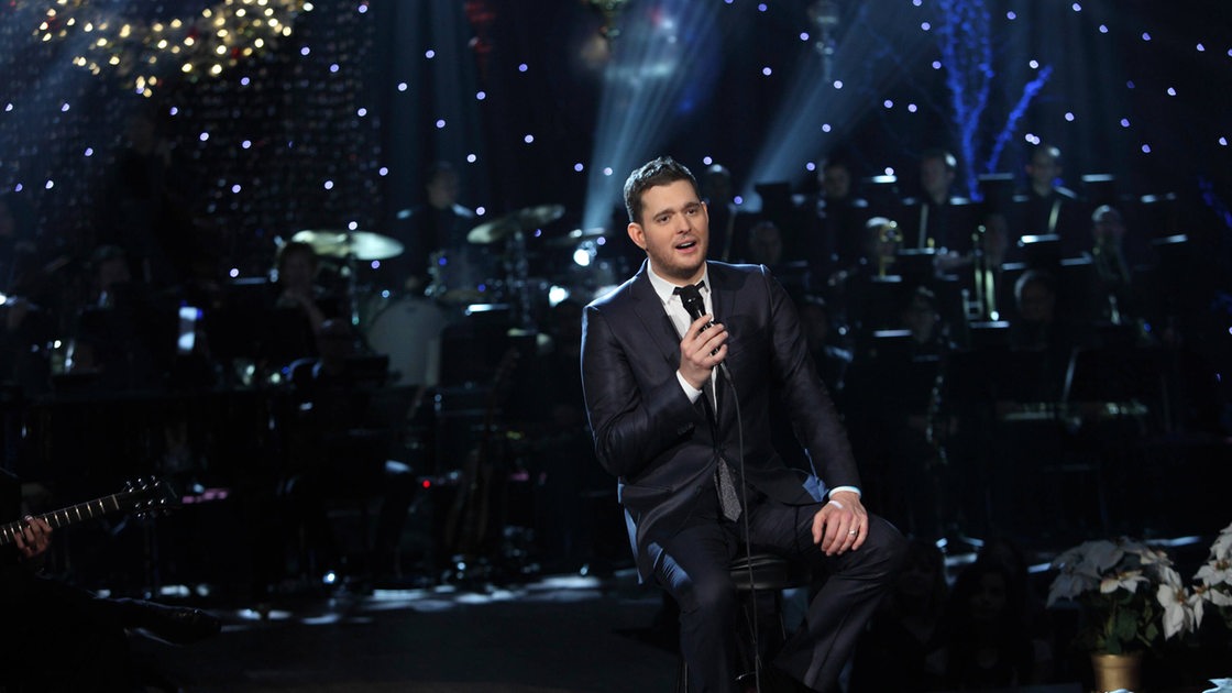 Michael Bublé sitzt auf einem Hocker auf einer Bühne und singt