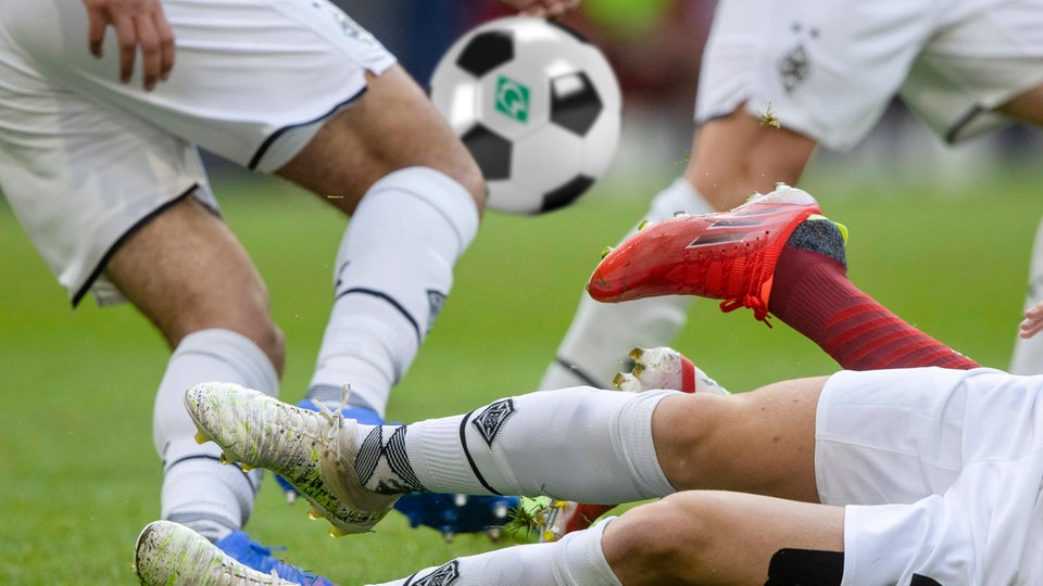 Verschiedene Beine von Fußballern, liegend und stehend, die um einen Ball mit Werder-Emblem kämpfen