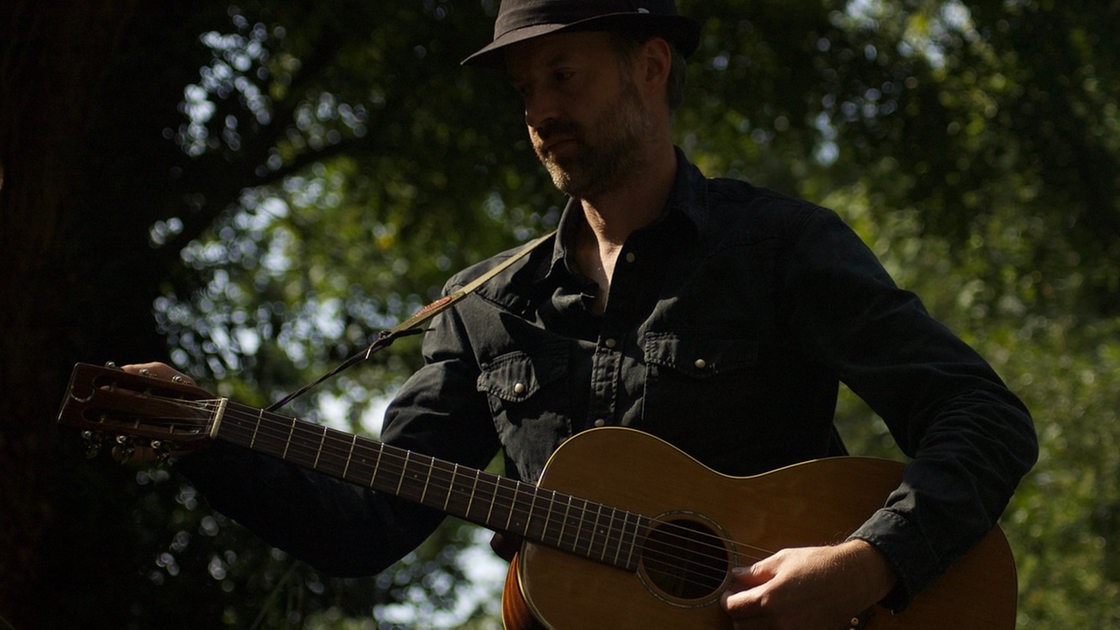 Sänger Jon Allen trägt einen schwarzen Hut und spielt Gitarre