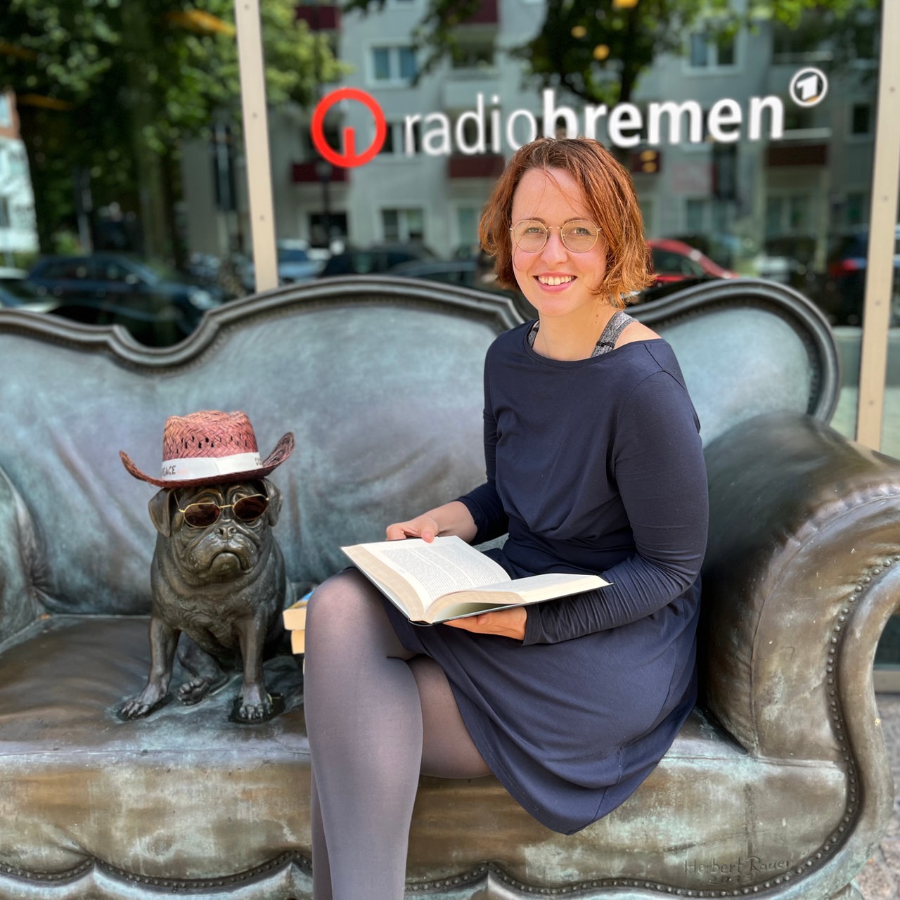Mirjam Benecke mit Buch auf dem bronzenen Loriot-Sofa mit Mops