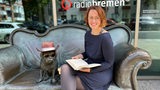 Mirjam Benecke mit Buch auf dem bronzenen Loriot-Sofa mit Mops