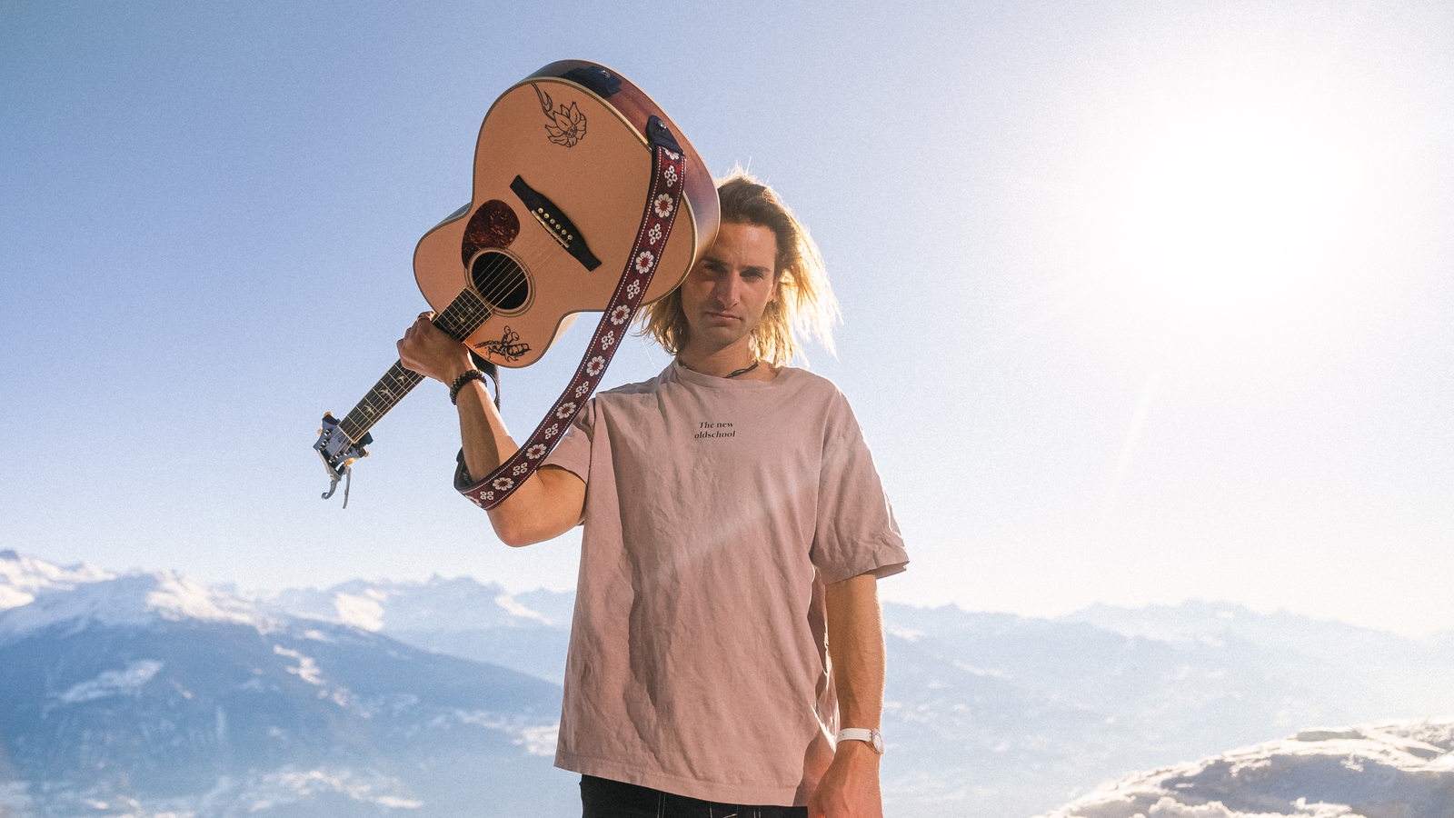 Der Musiker Pat Burgener steht mit Gitarre und T-Shirt in den Schweizer Alpen