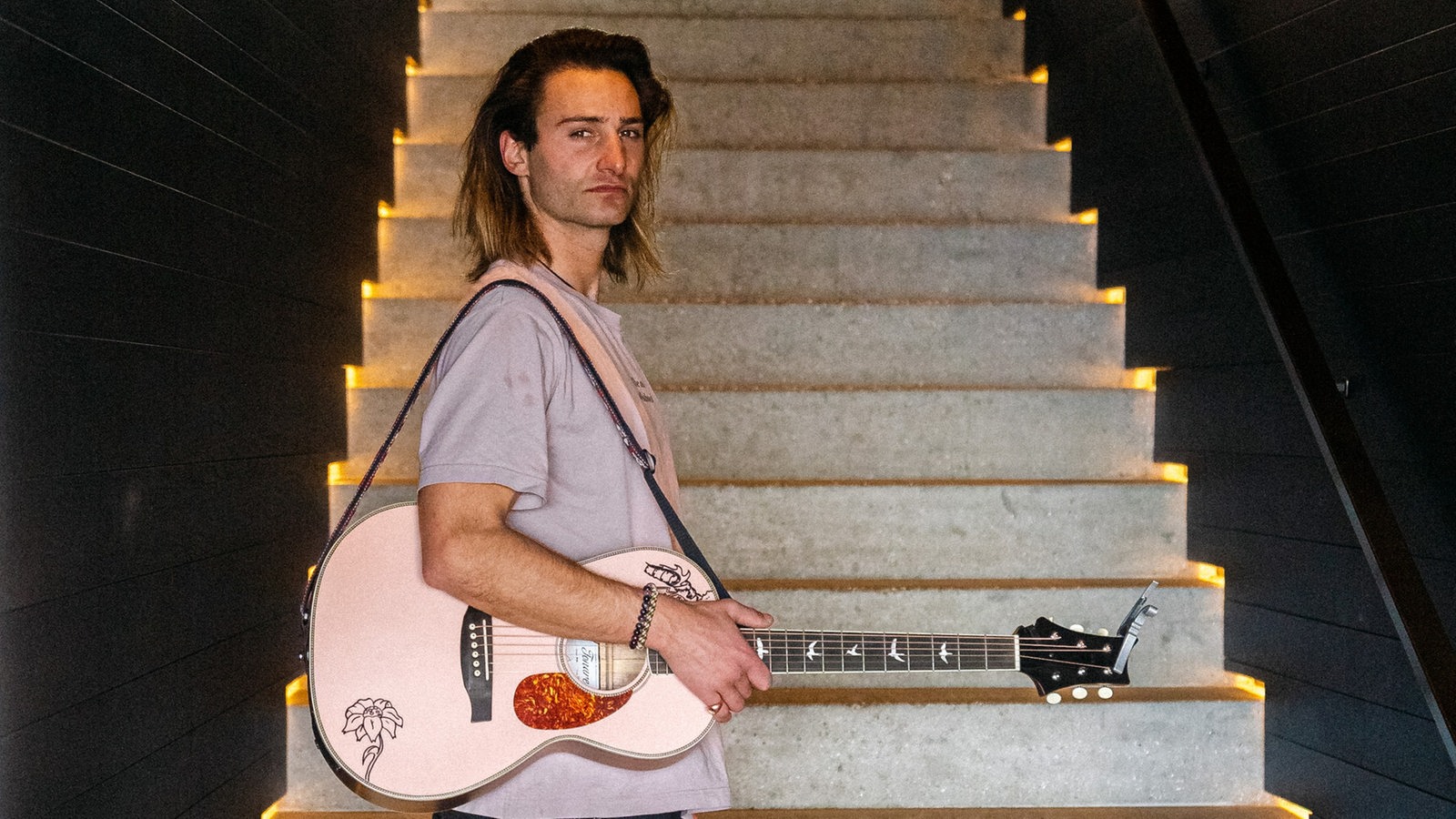 Pat Burgener steht mit einer Gitarre vor einer Treppe