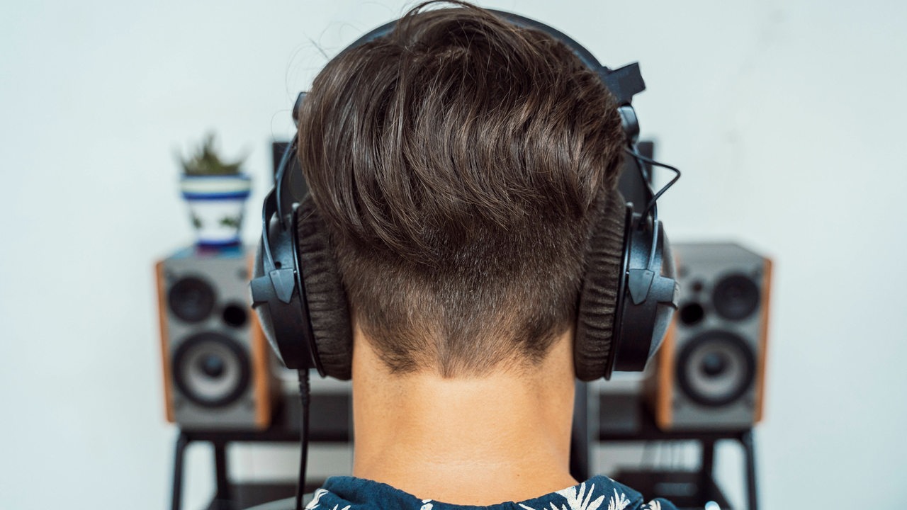 Ein Mann mit Kopfhörer von hinten, vor ihm eine Musikanlage (Symbolbild)