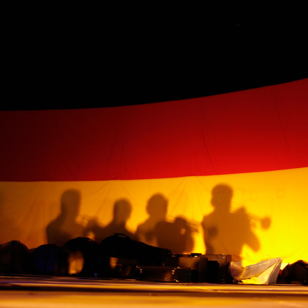 Auf einer Deutschlandfahne sieht man als Schatten 4 Trompeter