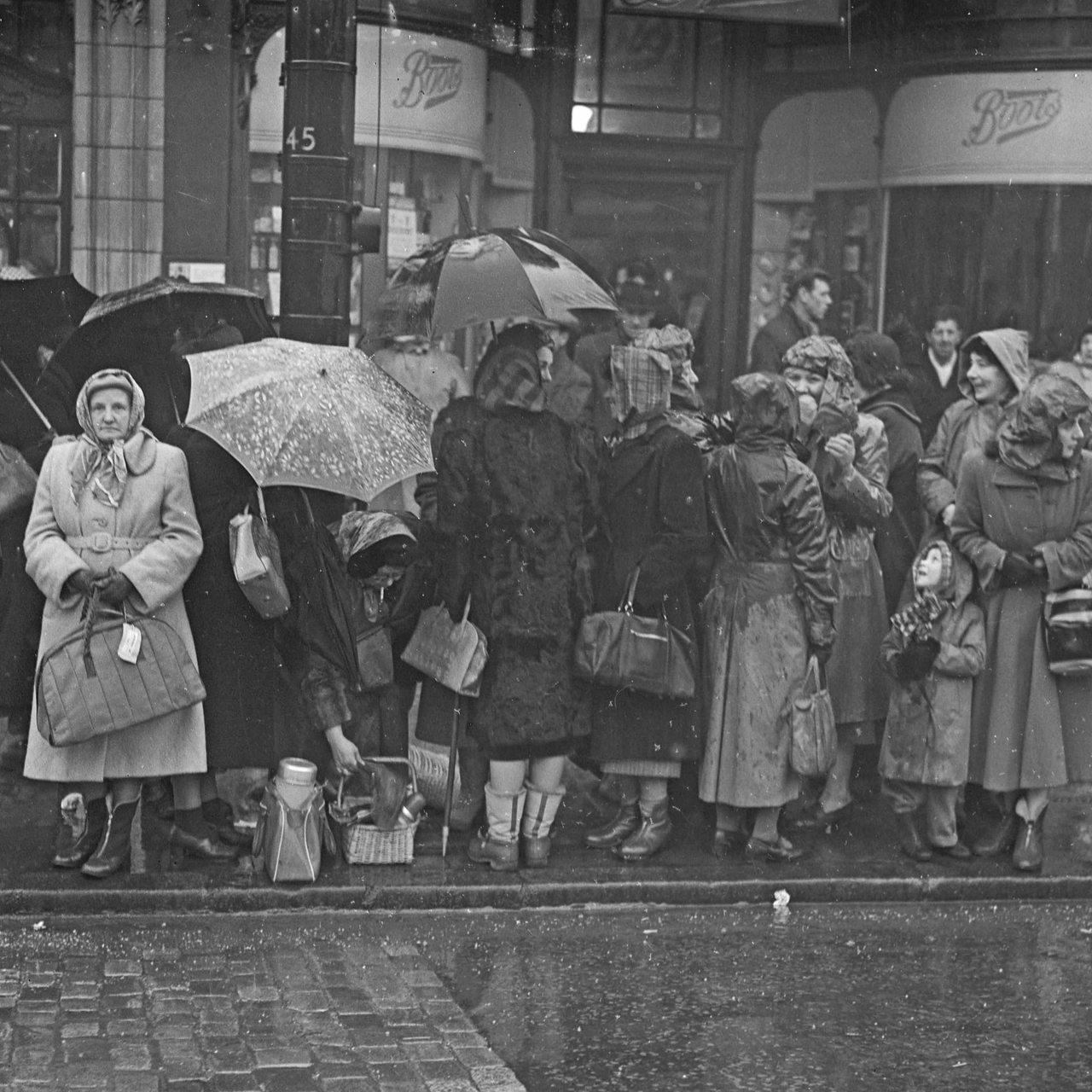 London 1952: Menschen mit Regenmänteln und Schirmen stehen an der Straße
