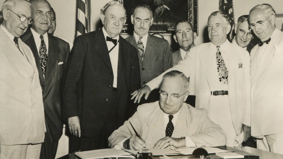 Präsident Truman unterschreibt 1949 den NATO Vertrag. Hinter ihm stehen weitere 9 Vertreter der NATO-Länder