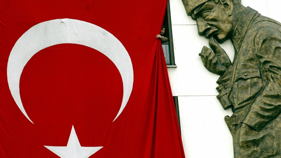 Neben einer riesigen Flagge der Türkei an einer Hauswand sieht man die Plastik des Staatsgründers Kemal Atatürk.